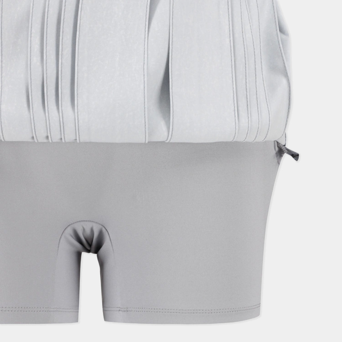 Close-up of a light gray two-piece garment, showing a pleated top section and matching fitted shorts with a front split opening, on a plain light background.