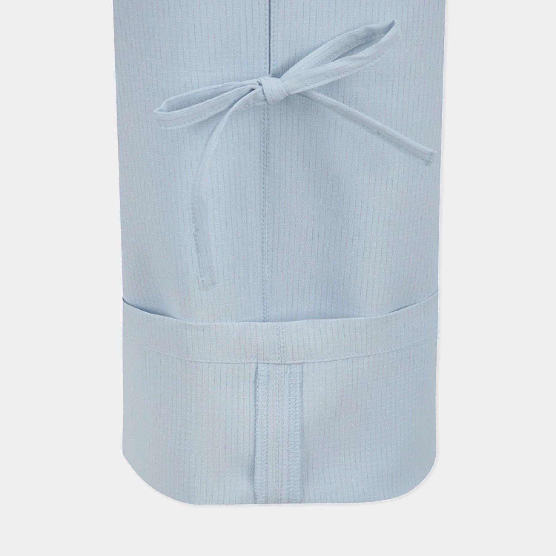 A close-up of a light blue scrub apron with a fine vertical stripe texture, featuring a front pocket and a matching fabric tie, set against a plain light gray background.