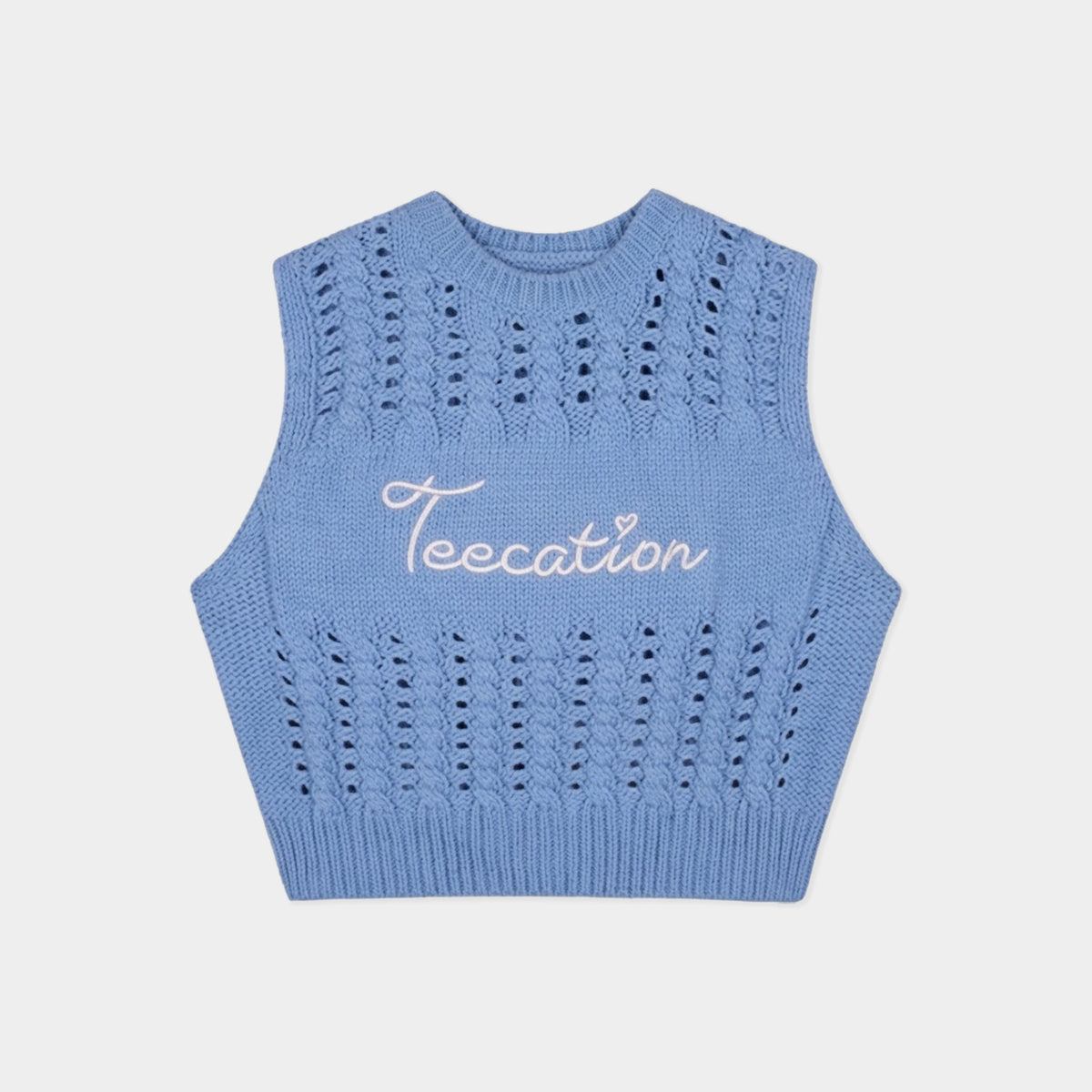A light blue sleeveless knit crop top sweater vest with a white cursive embroidered logo reading 'Teecation' on the chest, displayed flat against a light gray background.