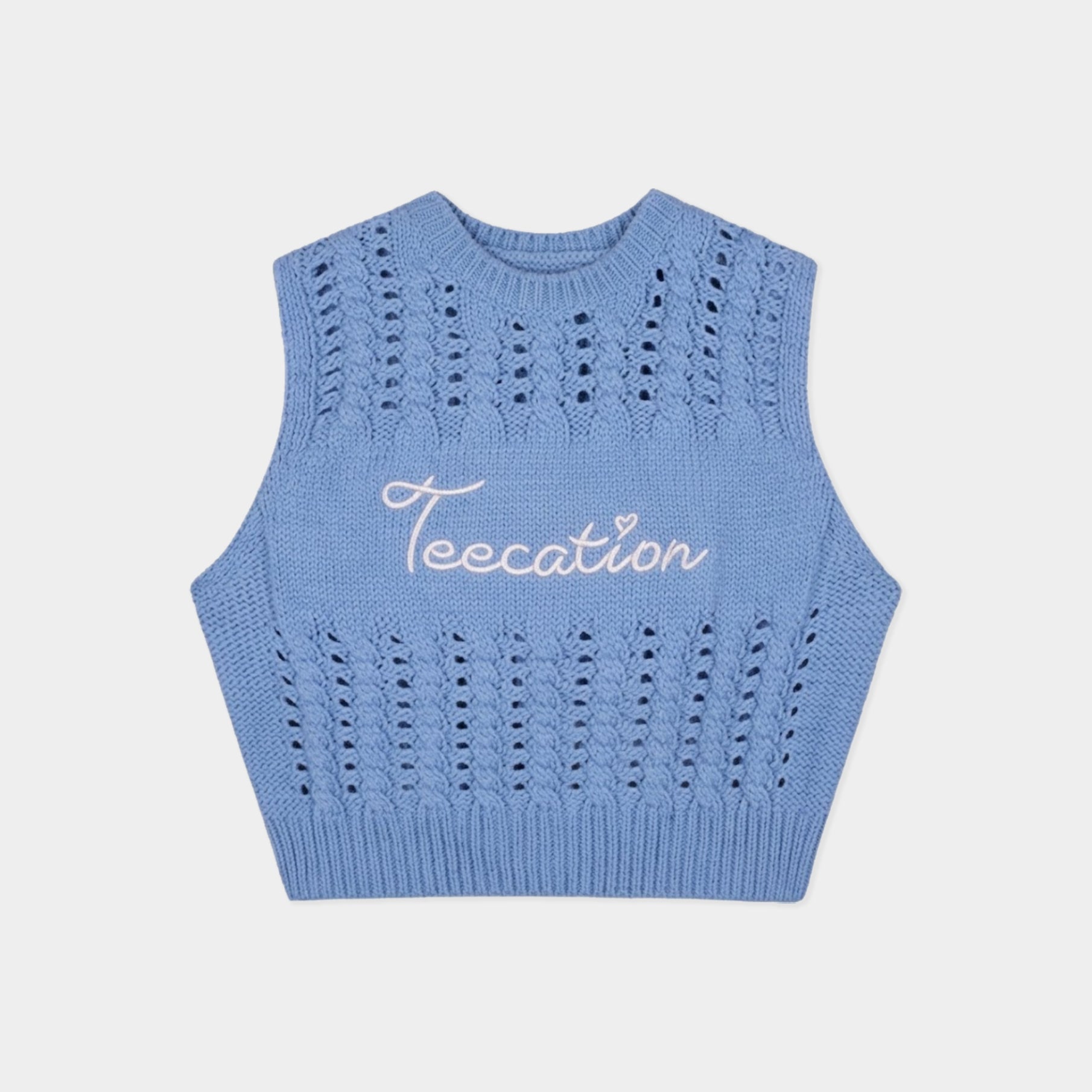 A light blue sleeveless knit crop top sweater vest with a white cursive embroidered logo reading 'Teecation' on the chest, displayed flat against a light gray background.