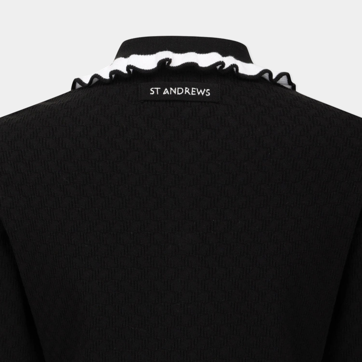 Close-up of the back of a black knit sweater with a white ruffled trim along the collar and a black label reading ST ANDREWS.
