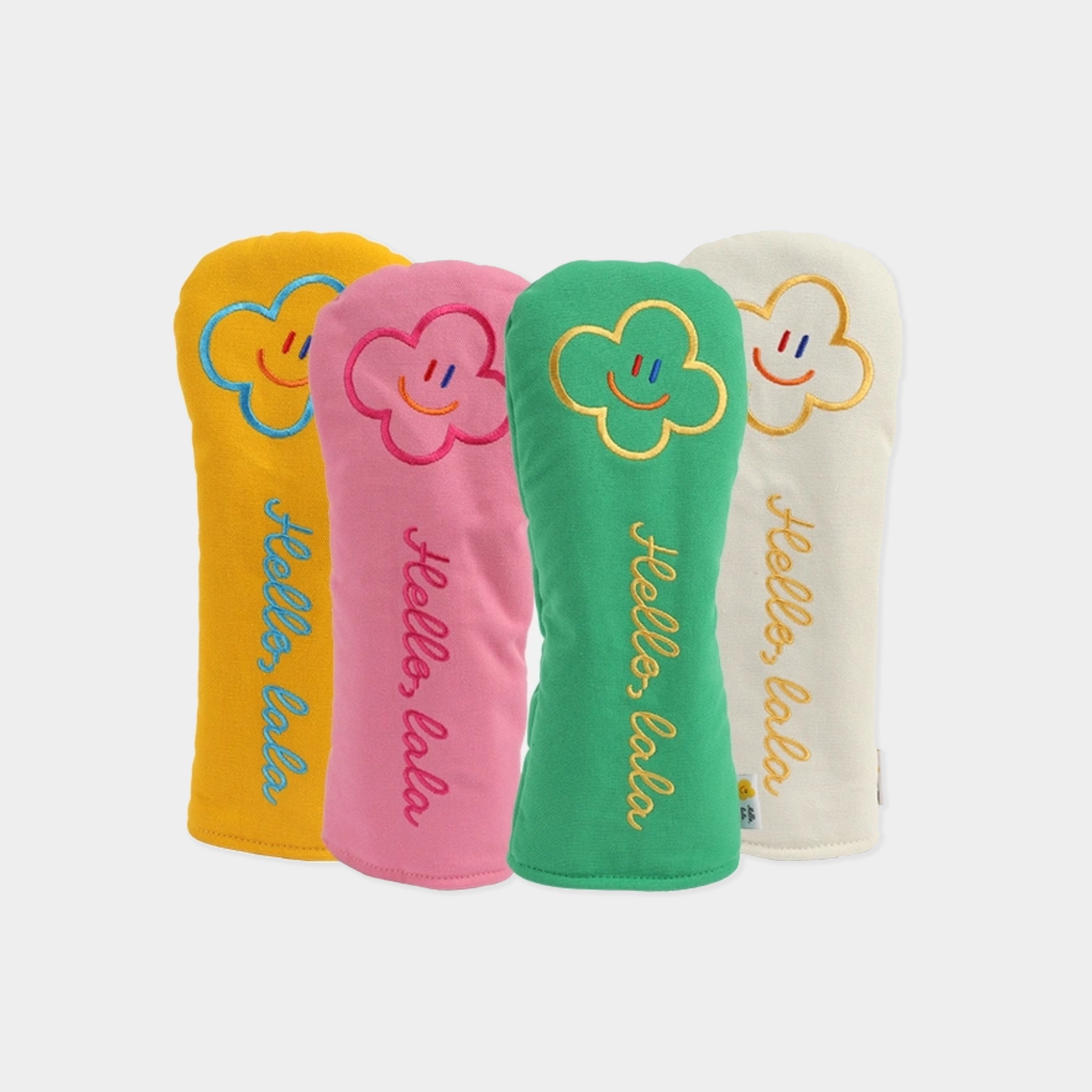 Four plush golf club headcovers in yellow, pink, green, and off-white, each featuring a smiling cloud face and the embroidered text 'Hello, kula.' on a light gray background.