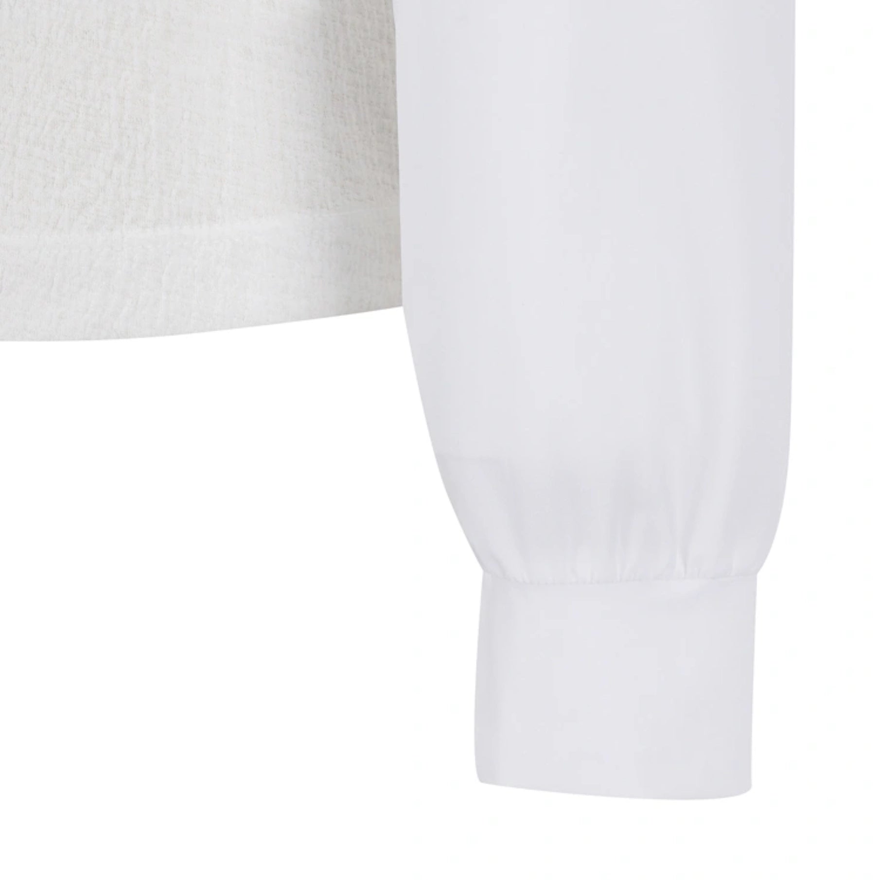 Close-up detail of a white long-sleeve top showing the sleeve cuff and part of the textured fabric body.