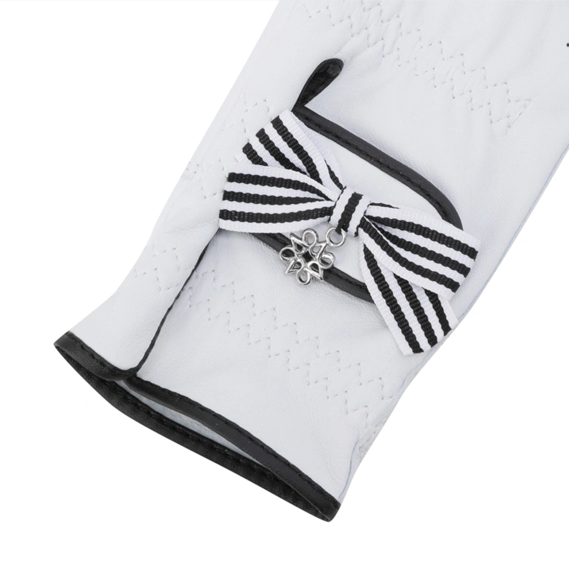 A close-up of a white golf glove featuring a black and white striped bow detail with a silver metal flower charm, set against a plain white background.