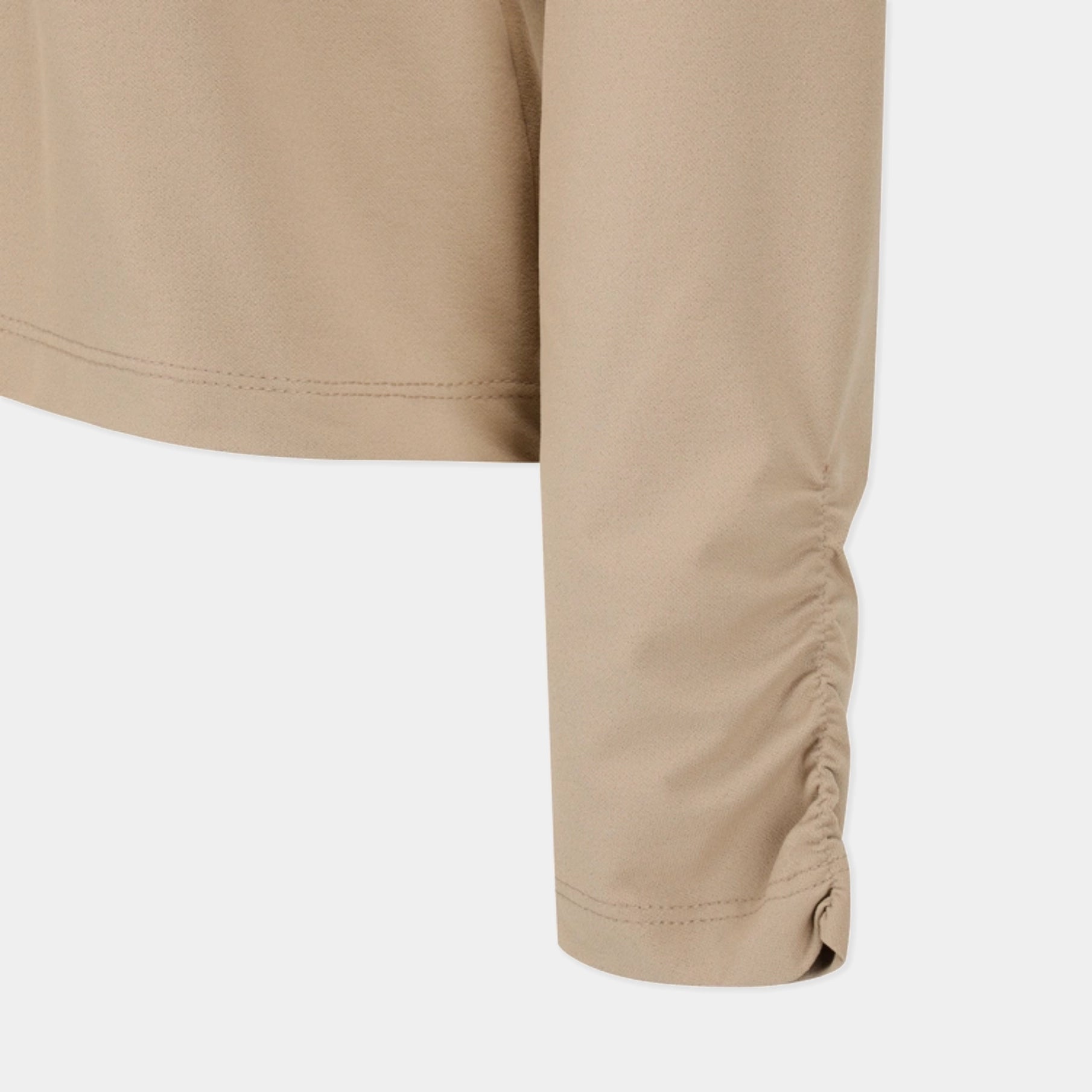 Close-up of a beige long-sleeve top showing the sleeve and side ruching detail against a light gray background.
