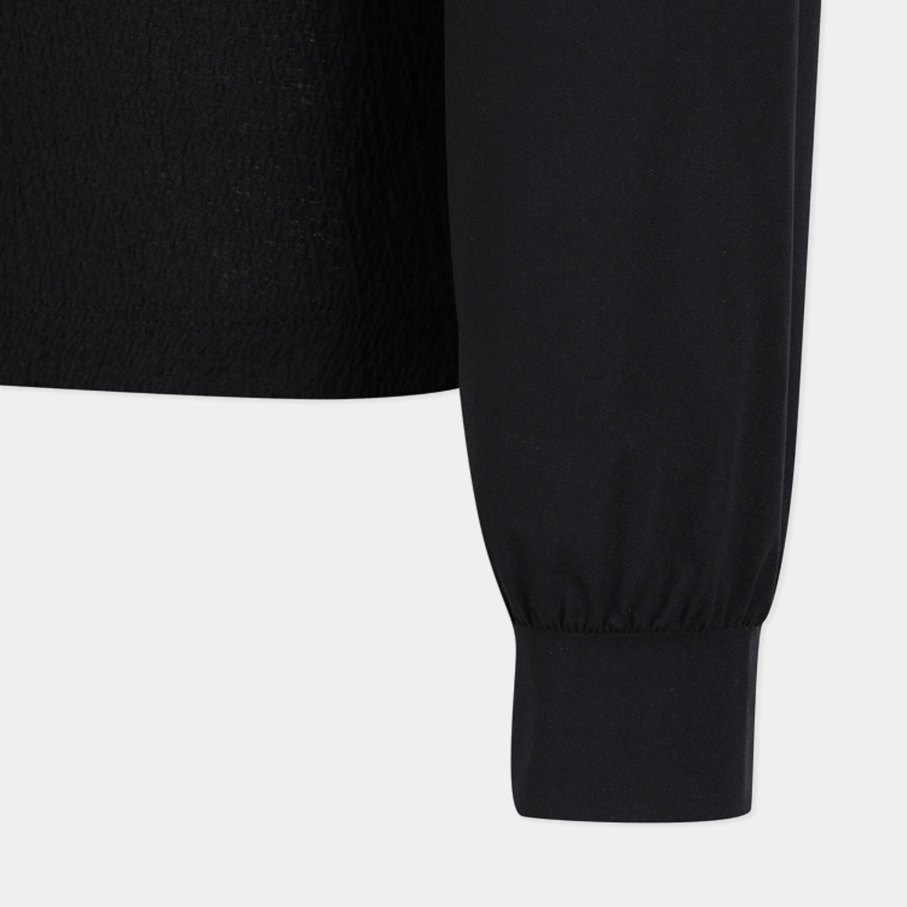 Close-up of a black long-sleeve top showing the sleeve and ribbed cuff against a light gray background.