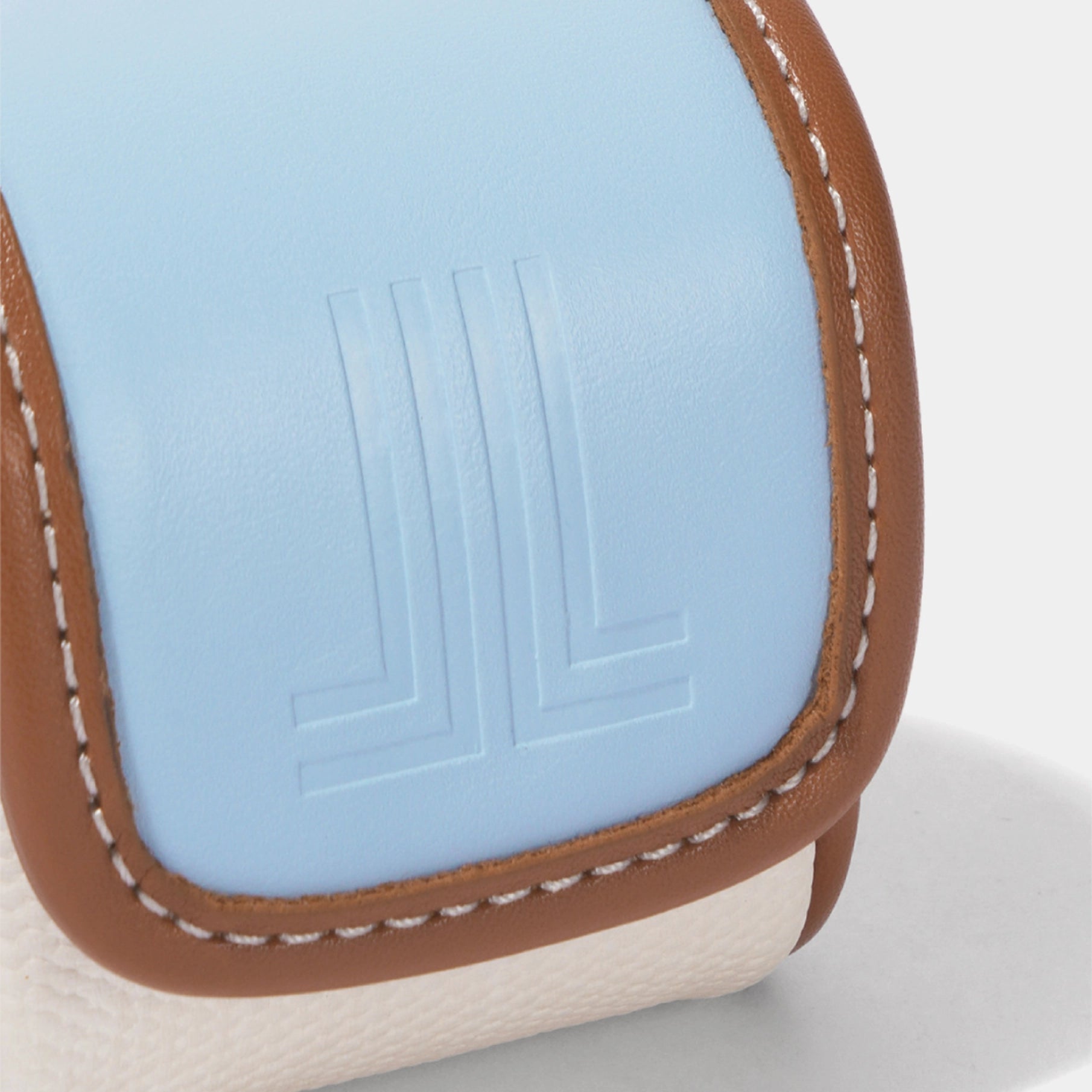 Close-up of a light blue leather pouch with brown leather trim, white stitching, and an embossed logo on a white textured surface.
