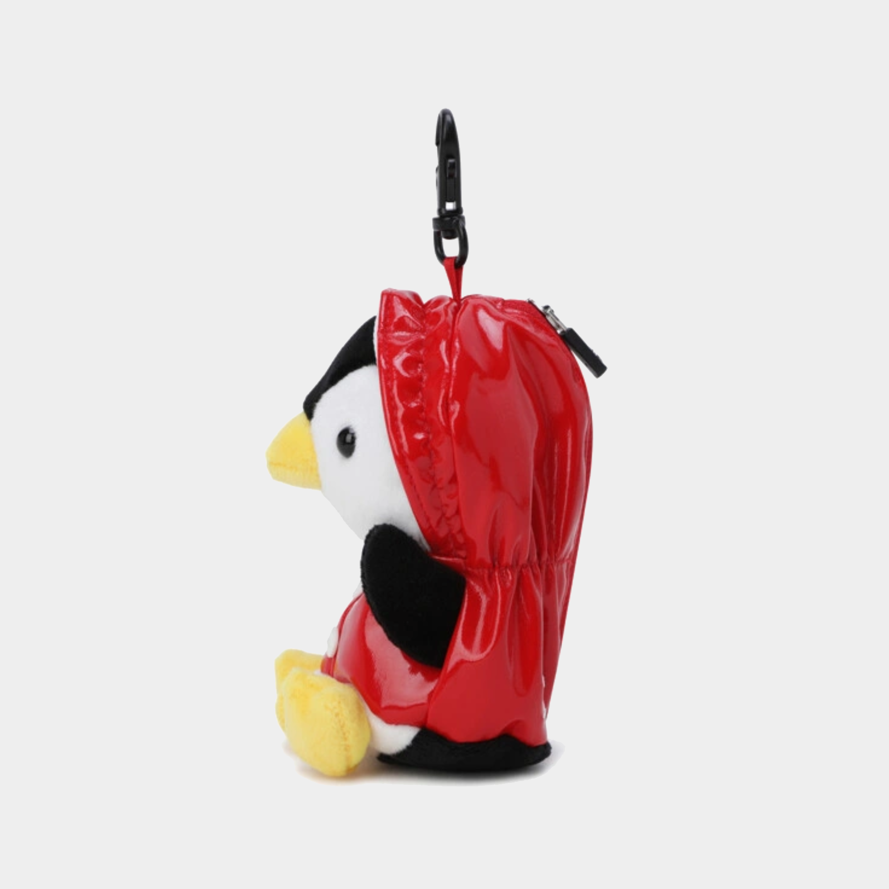 A small plush penguin keychain or bag charm wearing a shiny red hood, with a black carabiner clip at the top, shown on a light gray background.