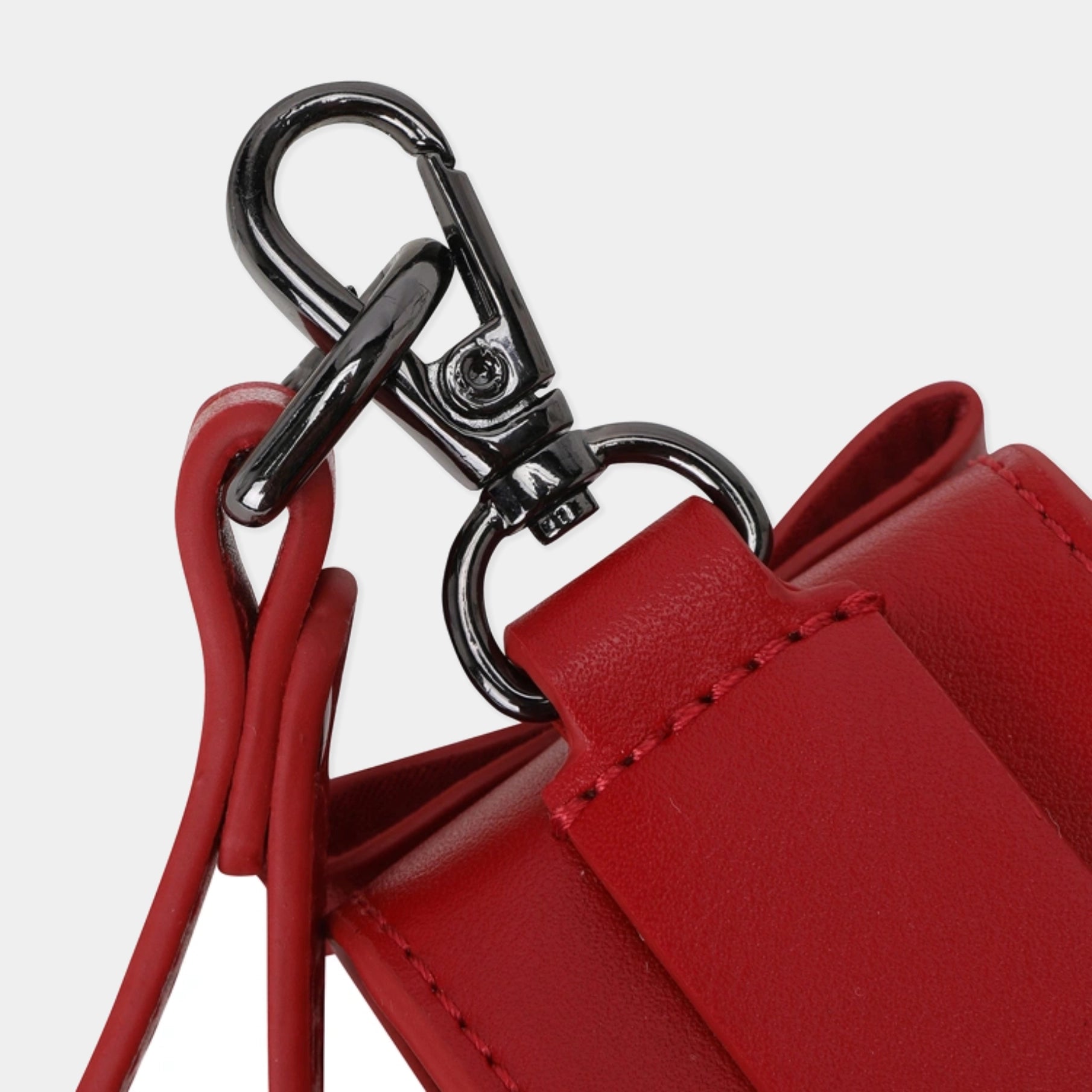 Close-up of a red leather bag strap with a black metal swivel clasp and ring hardware on a light gray background.