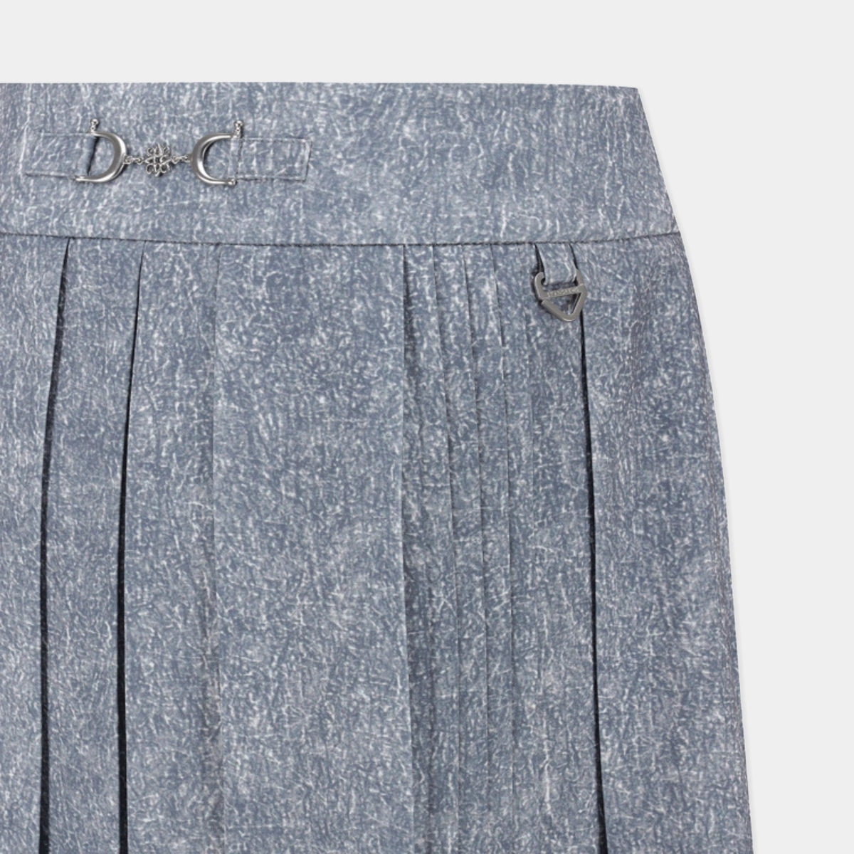 Close-up of a pleated skirt in a textured blue-gray fabric, featuring a decorative silver-tone horsebit detail on the waistband and a side pocket with a silver-tone ring closure.
