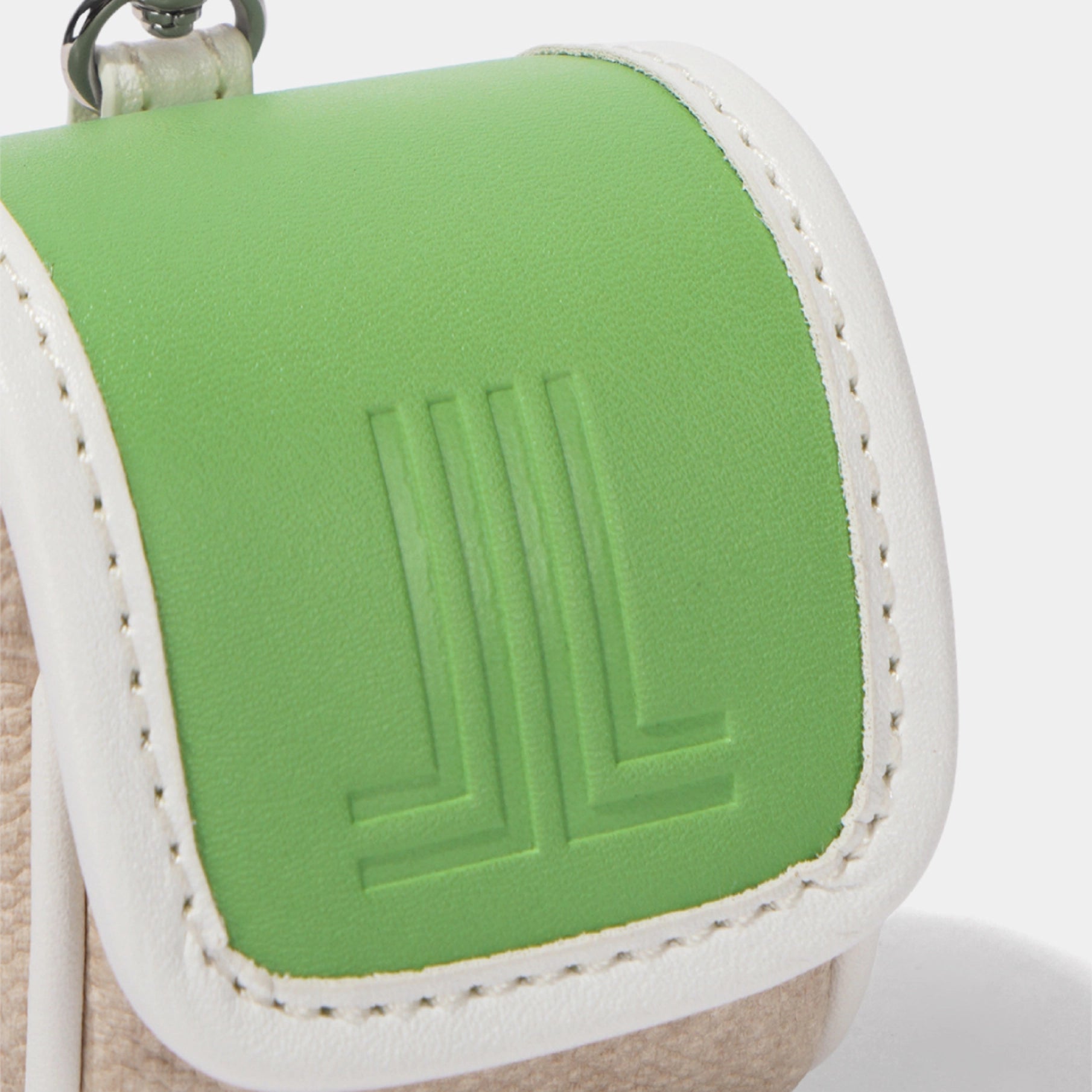 Close-up of a small pouch or wallet with a bright green flap featuring an embossed geometric logo, bordered by white stitching and a white leather trim, with a beige textured base visible underneath.