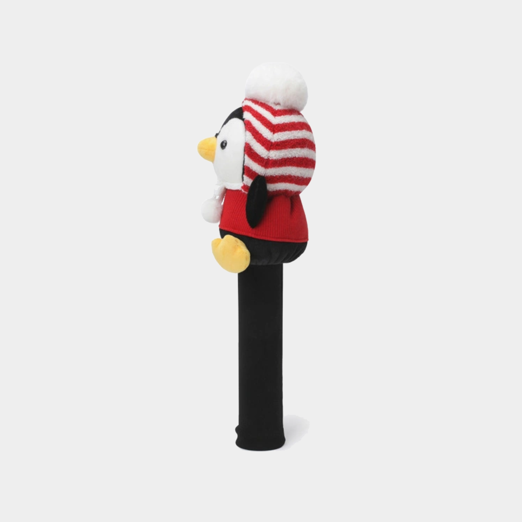 A plush penguin toy mounted on a black cylindrical stand, wearing a red and white striped knit hat with a white pom-pom and a red outfit, photographed against a light gray background.