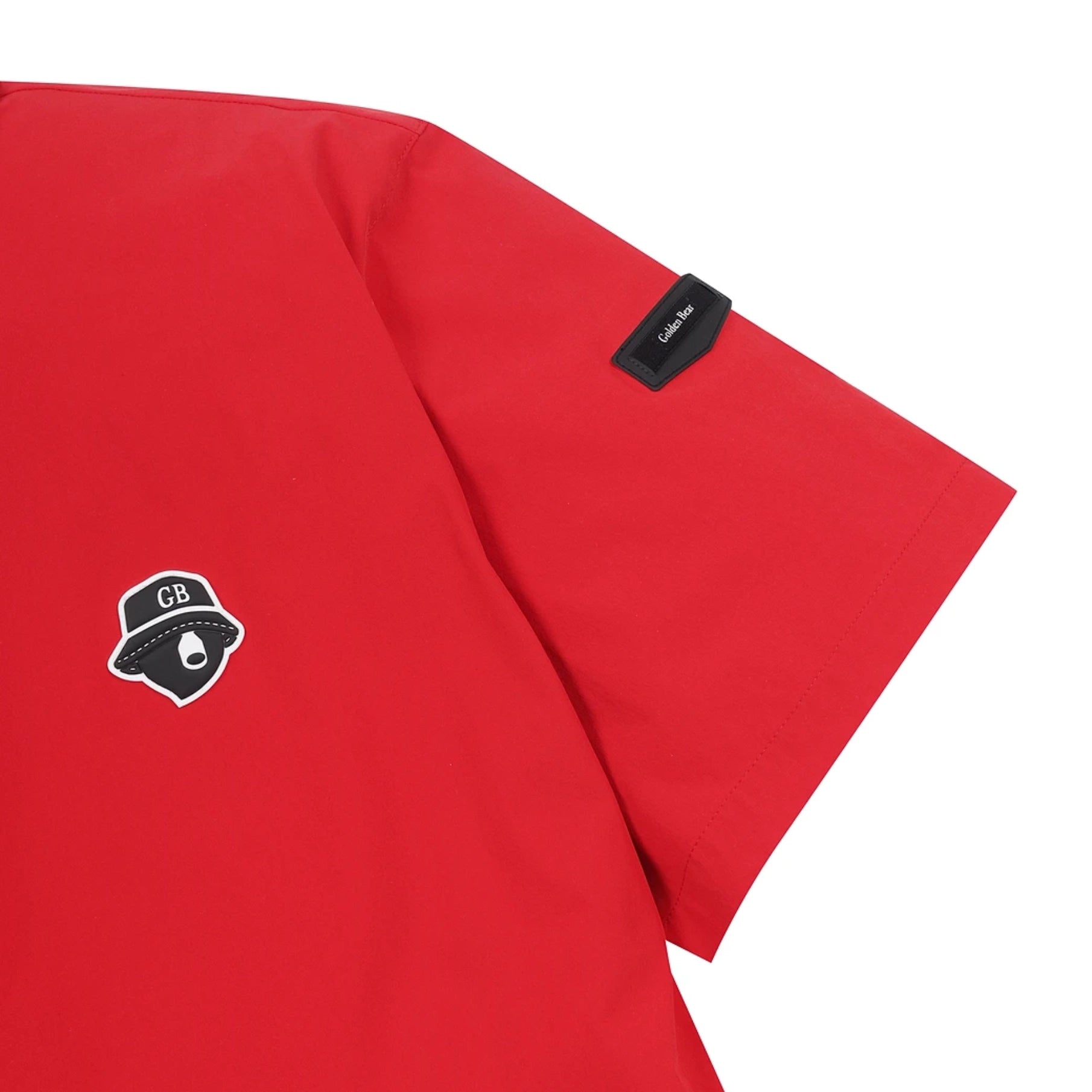 Close-up of a bright red short-sleeve shirt showing the sleeve with a black brand tag and a black chest patch featuring a hat graphic with the letters CB.