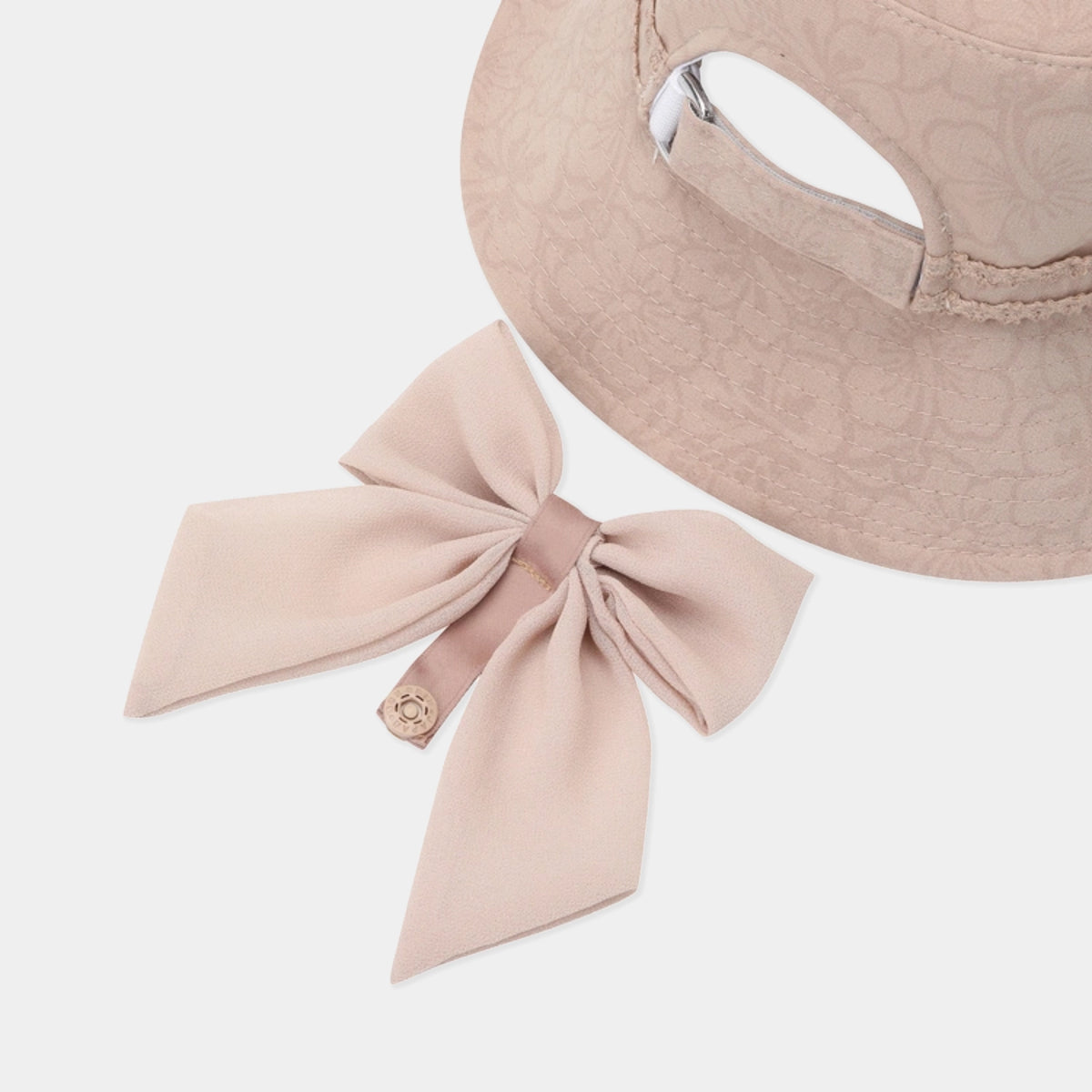 A pale blush pink sun hat with a matching fabric bow accessory and a small decorative button, photographed on a clean light gray background.