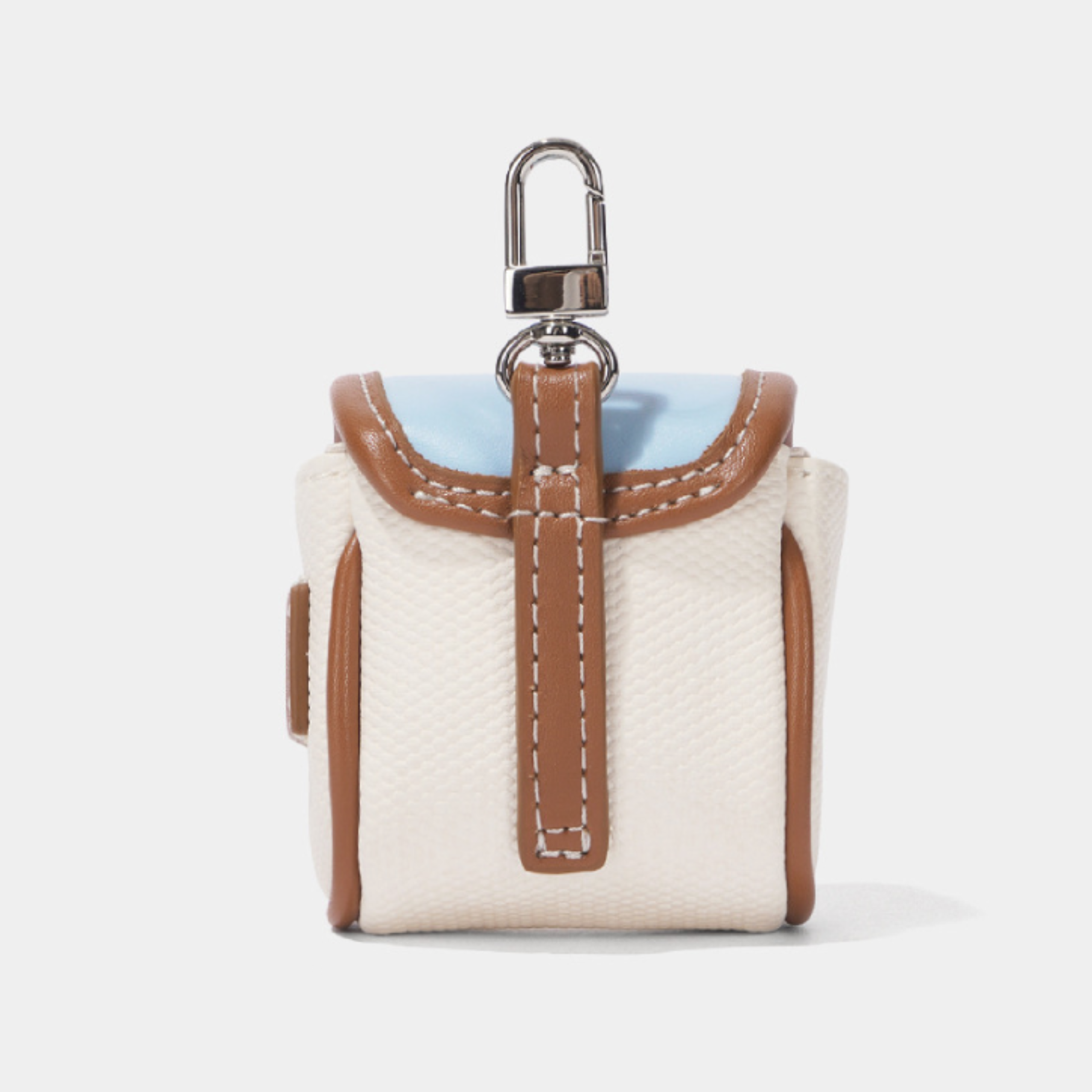 A small structured camera bag or pouch in off-white textured material with tan leather trim, a light blue top panel, and a silver metal clip, shown on a clean light gray background.