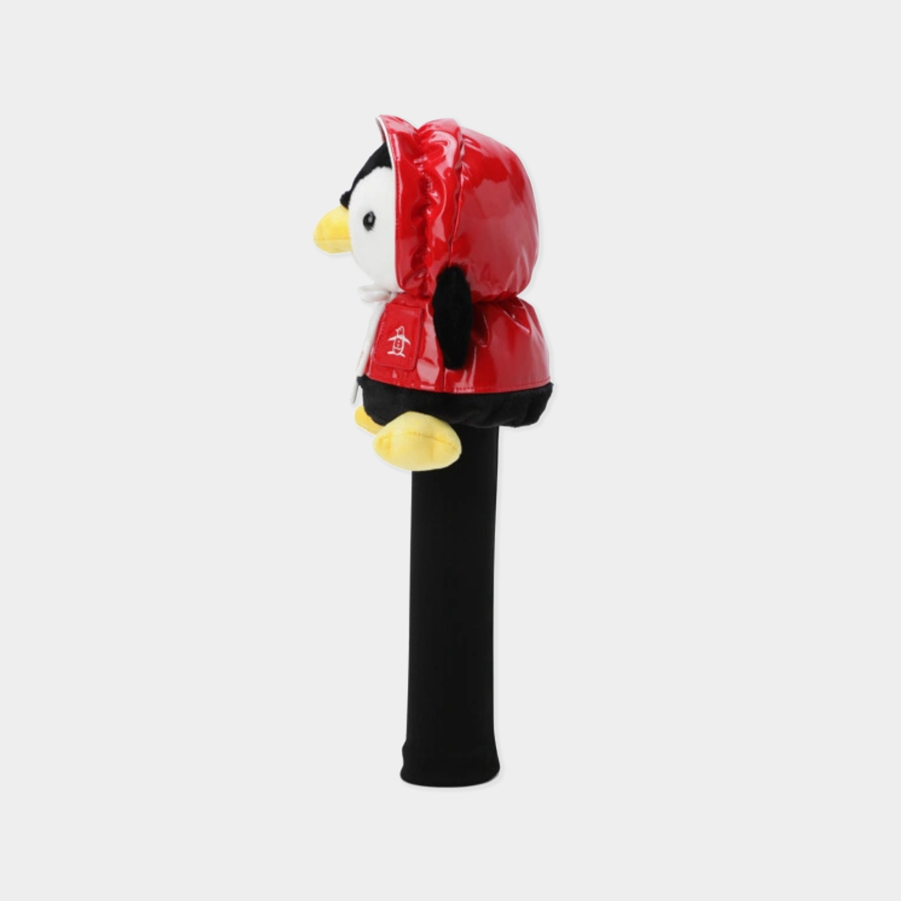 A golf club headcover featuring a plush penguin dressed in a shiny red hooded jacket, standing upright on a black sleeve against a light gray background.