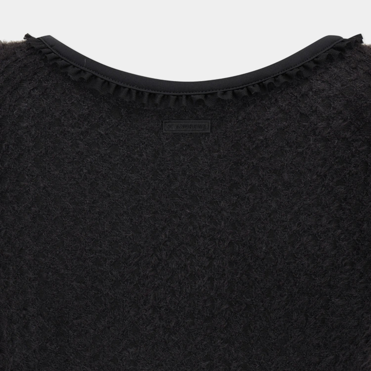 Close-up of a black textured knit top with a ruffled trim along the neckline and a small rectangular brand label at the center.
