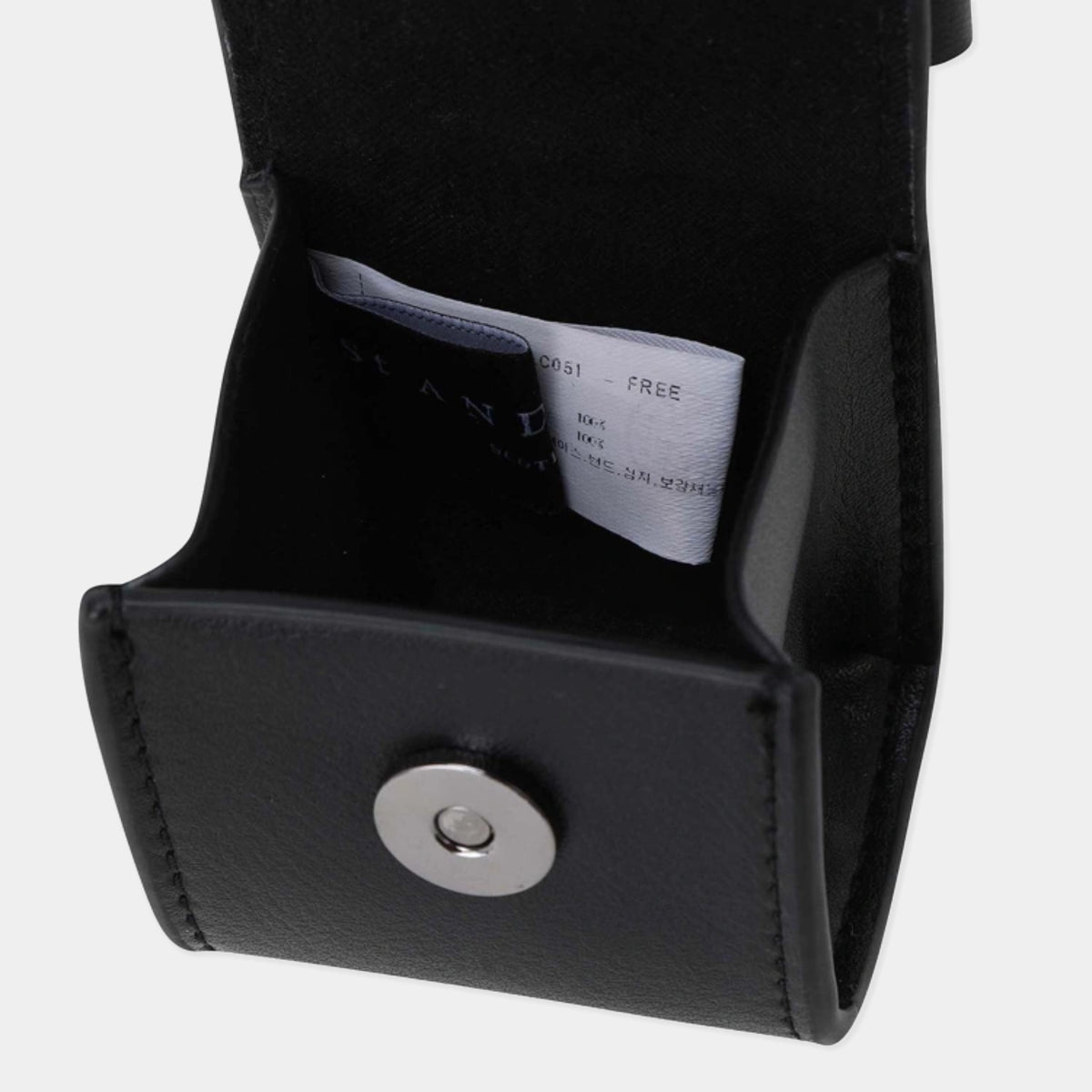 Close-up of a black leather or faux-leather pouch with a silver snap button, showing a white interior tag with text.