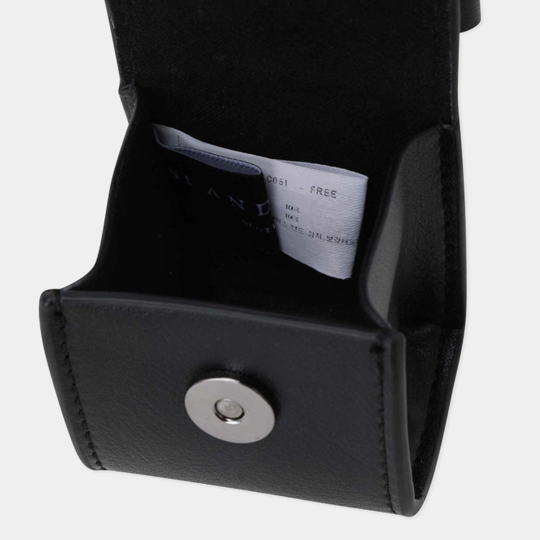 Close-up of a black leather or faux-leather pouch with a silver snap button, showing a white interior tag with text.