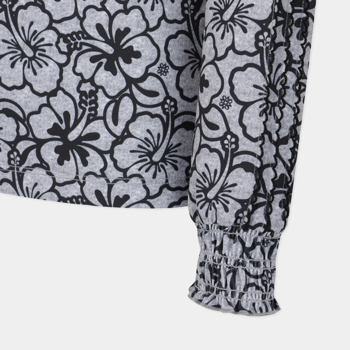 Close-up of a long-sleeve top with a black and gray floral hibiscus pattern and a smocked elasticated cuff on the sleeve, shown against a light gray background.