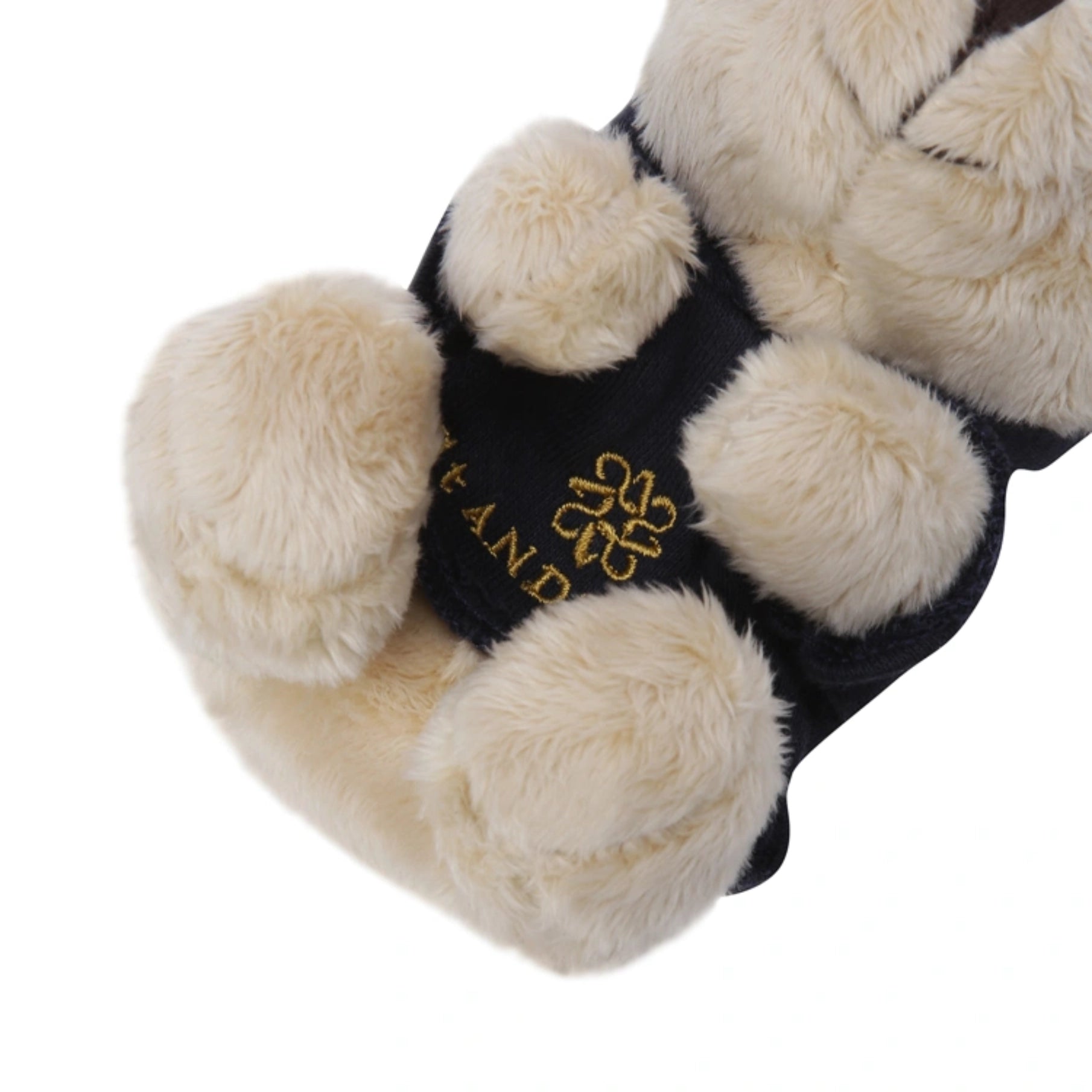 Close-up of a plush animal paw toy or accessory with cream faux-fur pads and a dark navy center band featuring gold embroidered text and a flower-like logo.