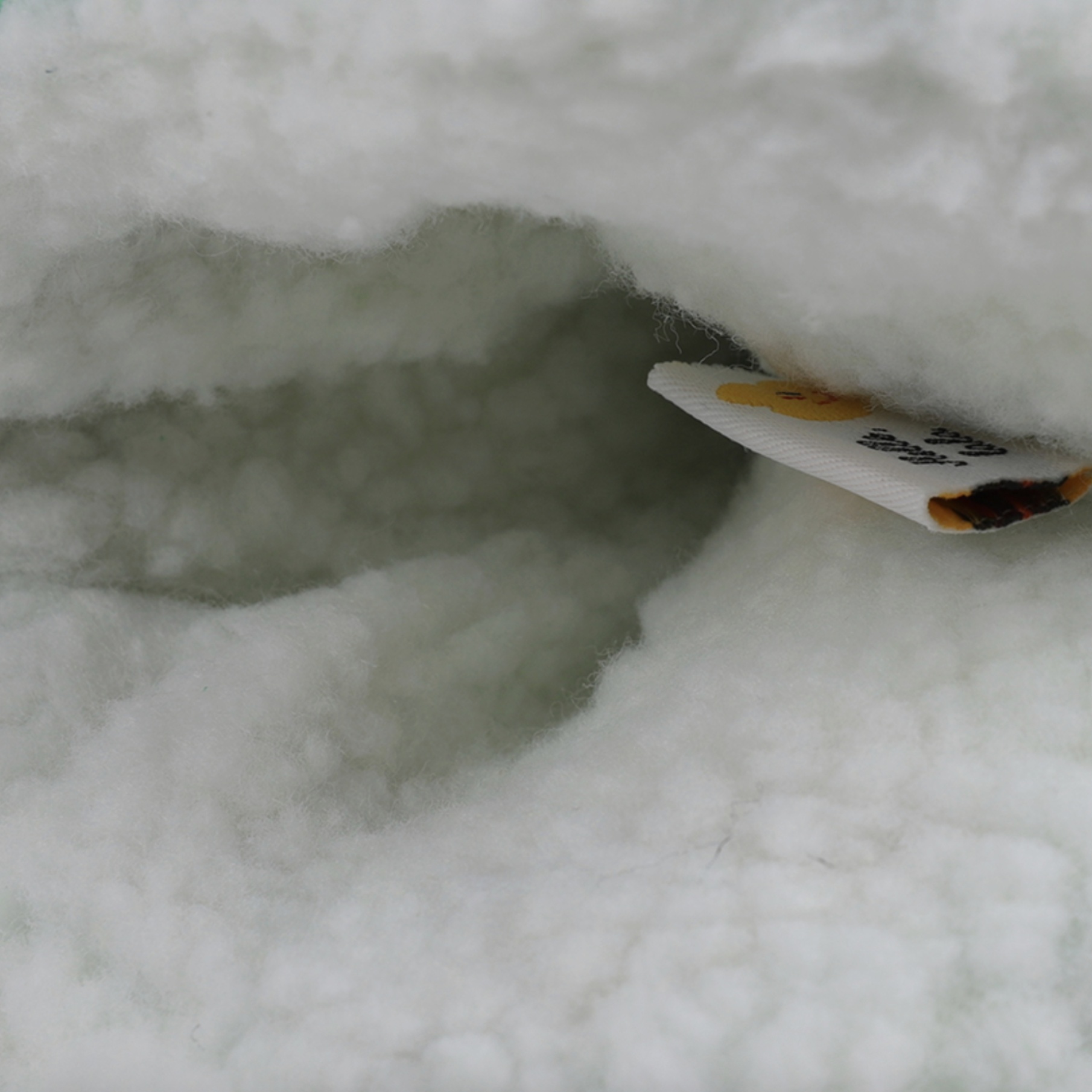 Close-up of white fluffy faux fur or fleece fabric with a small white fabric tag partially visible on the right side.