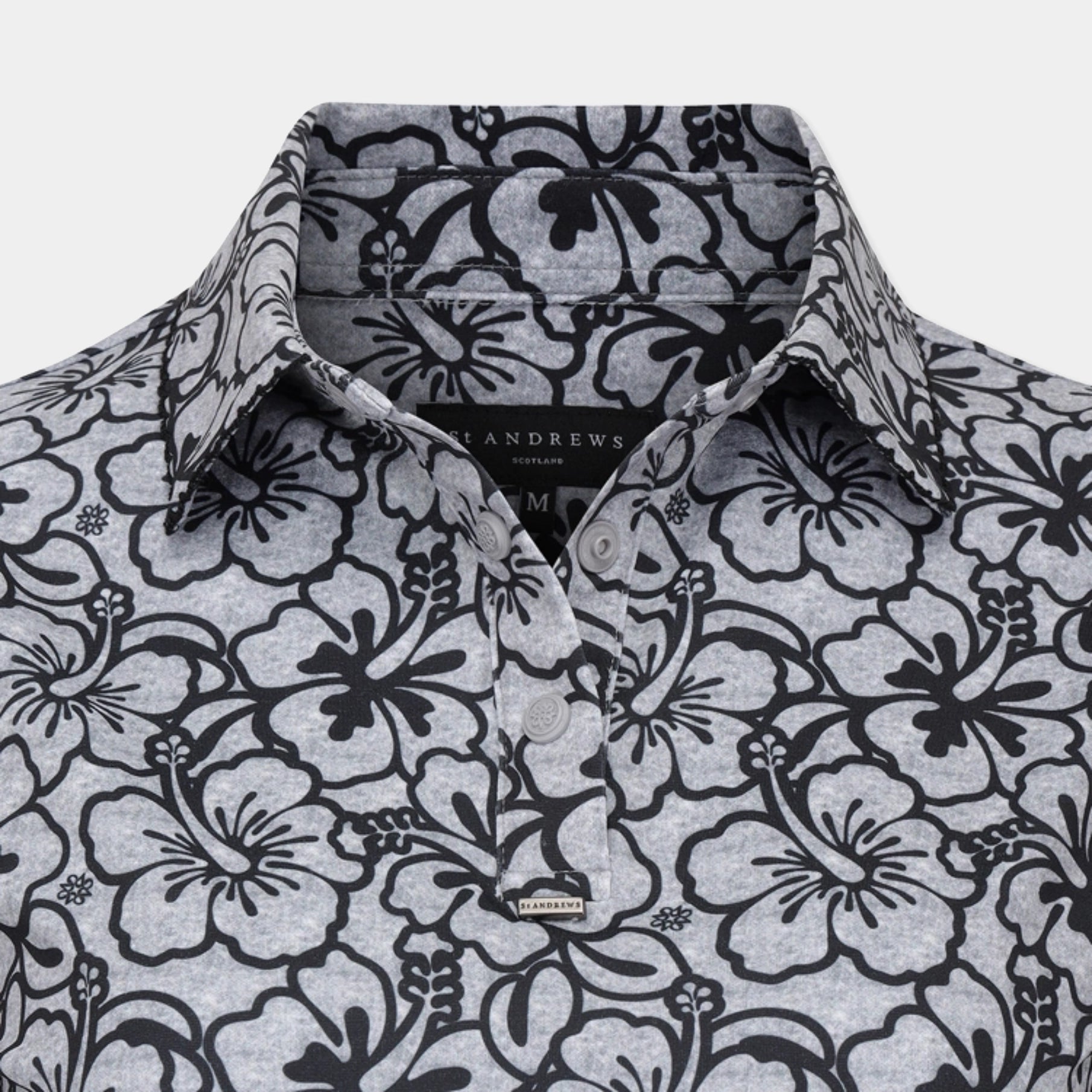 Close-up of a collared button-up shirt by Andrews London featuring a black floral hibiscus pattern on a heather gray fabric, with a visible brand label at the collar and chest.