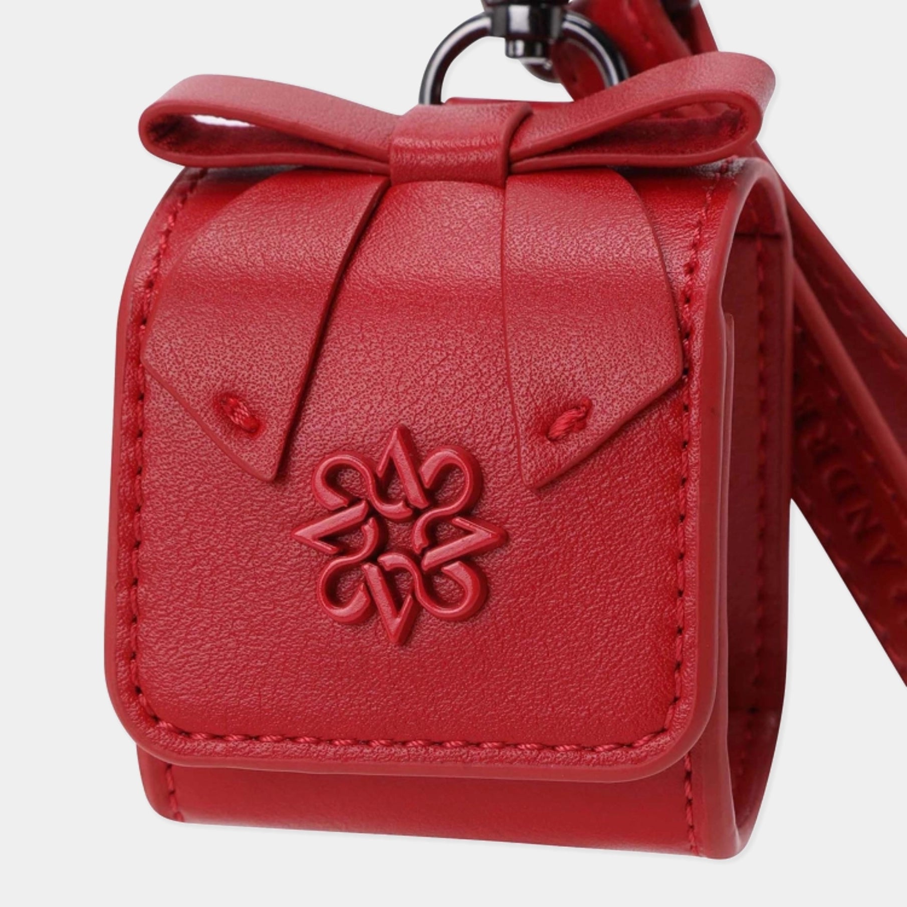 A red textured leather key case with a bow on top, a debossed floral monogram on the front, and a strap attached, shown against a light gray background.