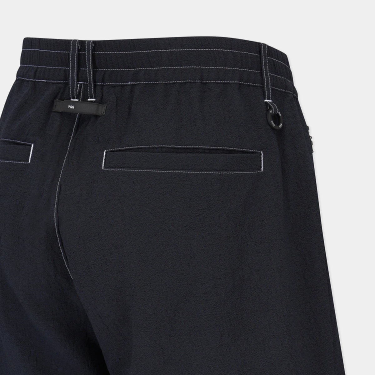 Close-up of the back waistband and pockets of black trousers, showing contrast stitching, belt loops, and a black fabric tag on the left side.
