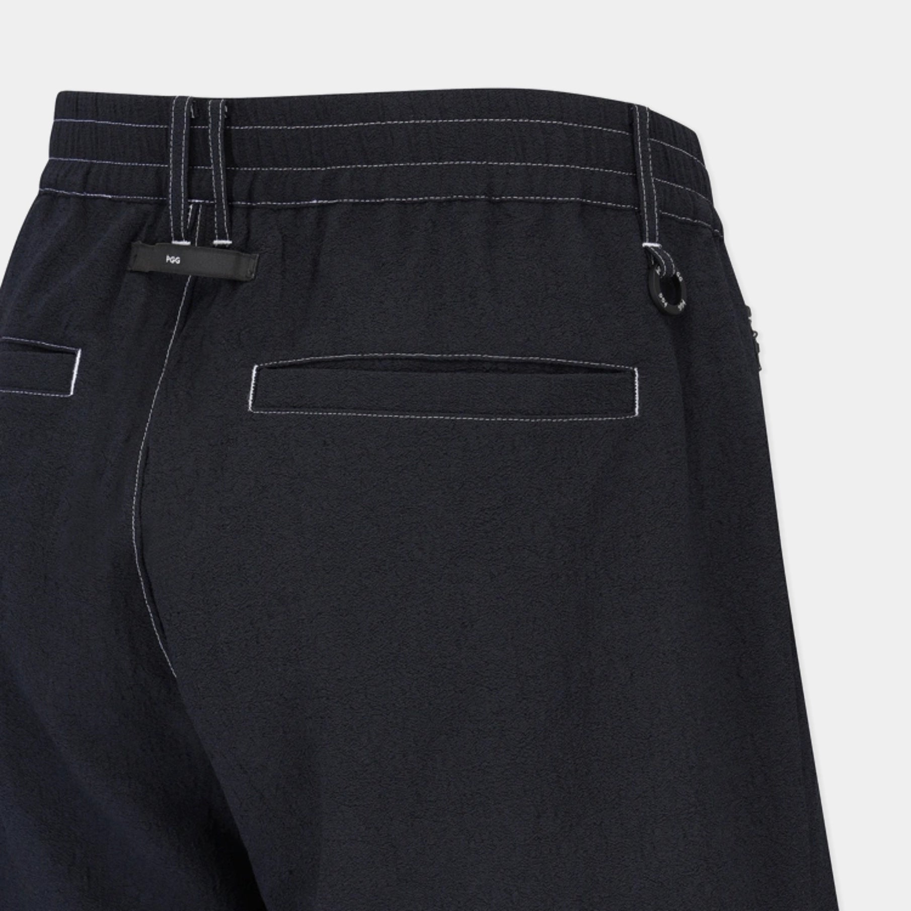 Close-up of the back waistband and pockets of black trousers, showing contrast stitching, belt loops, and a black fabric tag on the left side.