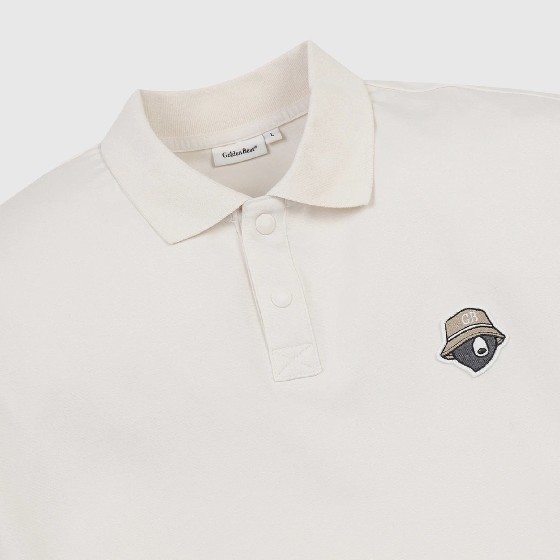 An off-white polo shirt by Caldas Bar, featuring a small embroidered bear wearing a hat with a 'GB' logo on the left chest, set against a clean, light gray background.