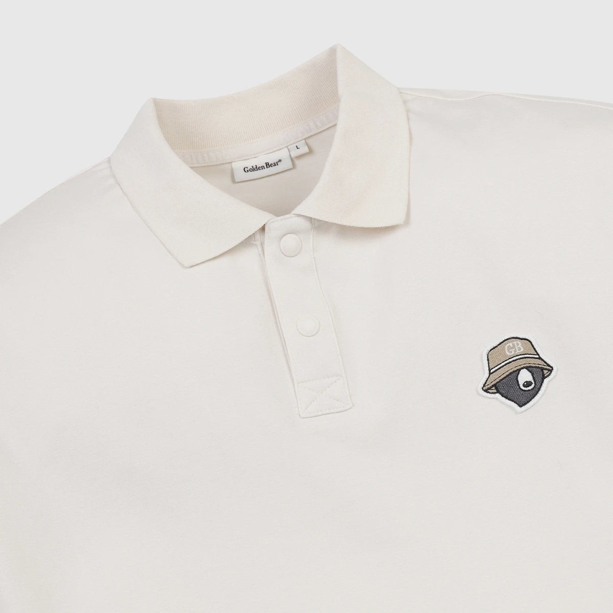 An off-white polo shirt by Caldas Bar, featuring a small embroidered bear wearing a hat with a 'GB' logo on the left chest, set against a clean, light gray background.