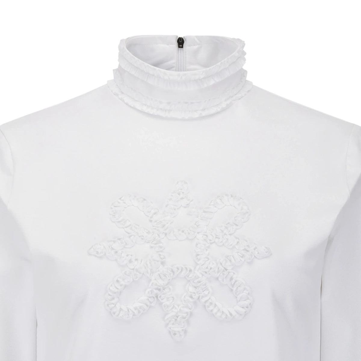 White long-sleeve top with a high ruffled mock neck and a large textured ruffled snowflake or floral applique on the chest.