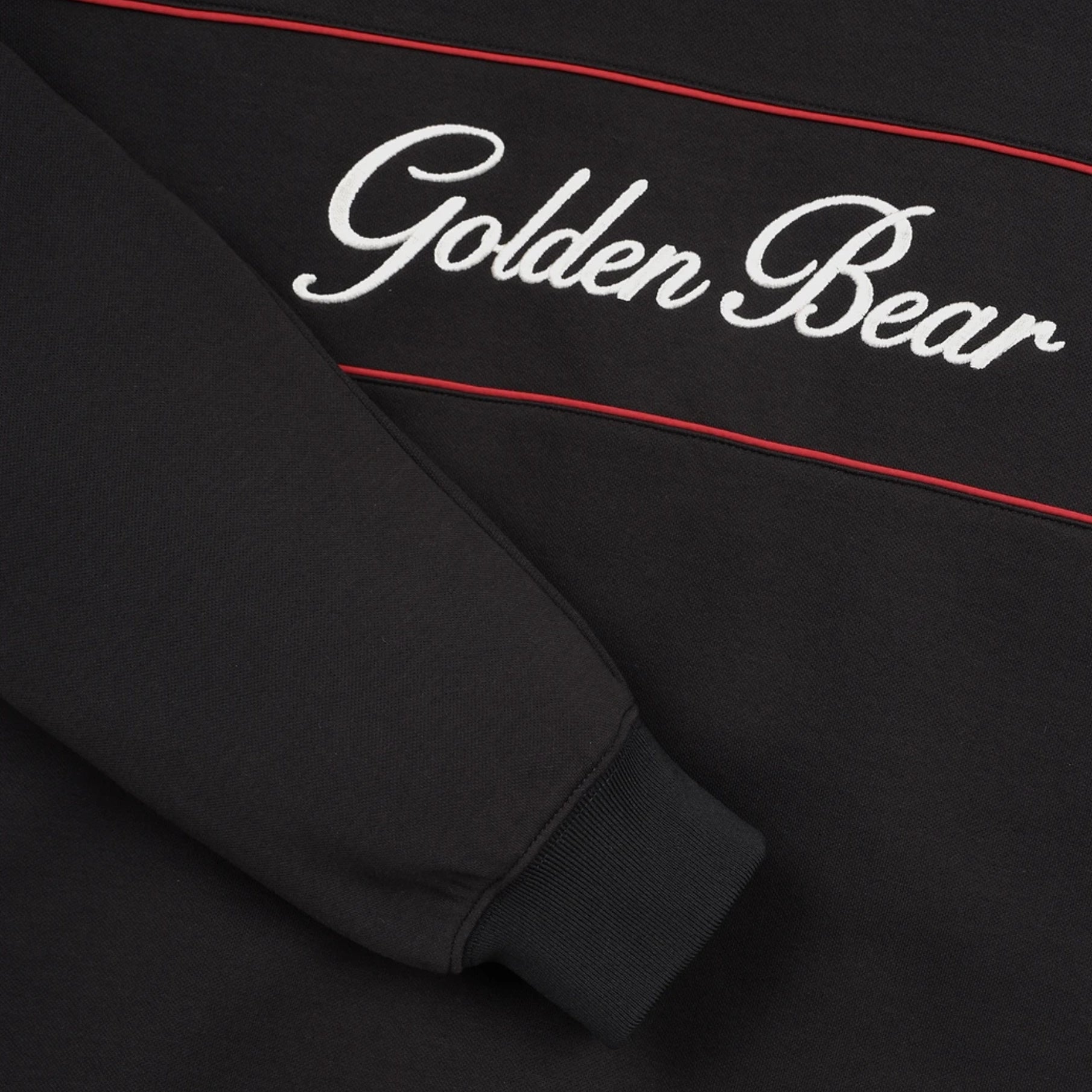 Close-up of a black sweatshirt featuring white cursive 'Golden Bear' embroidery and thin red accent lines.