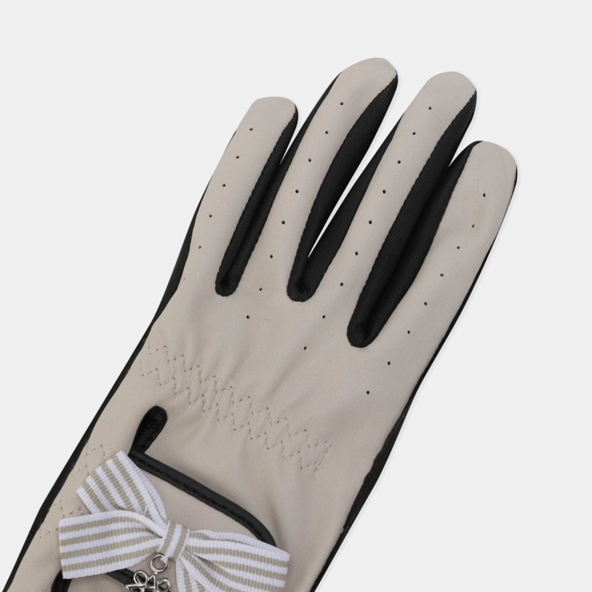 A single light beige glove with black trim and a striped white-and-beige ribbon bow with a small silver charm, shown on a light gray background.