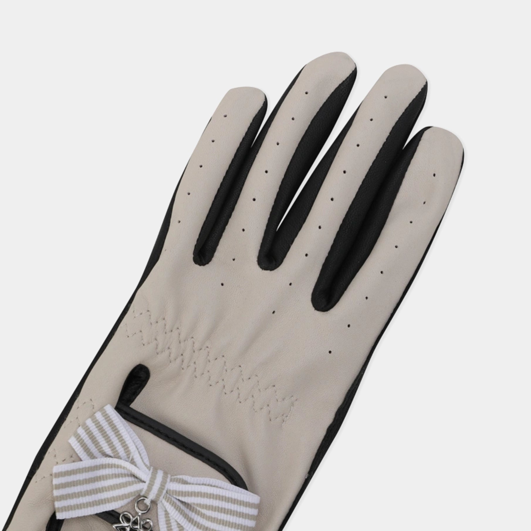 A single light beige glove with black trim and a striped white-and-beige ribbon bow with a small silver charm, shown on a light gray background.
