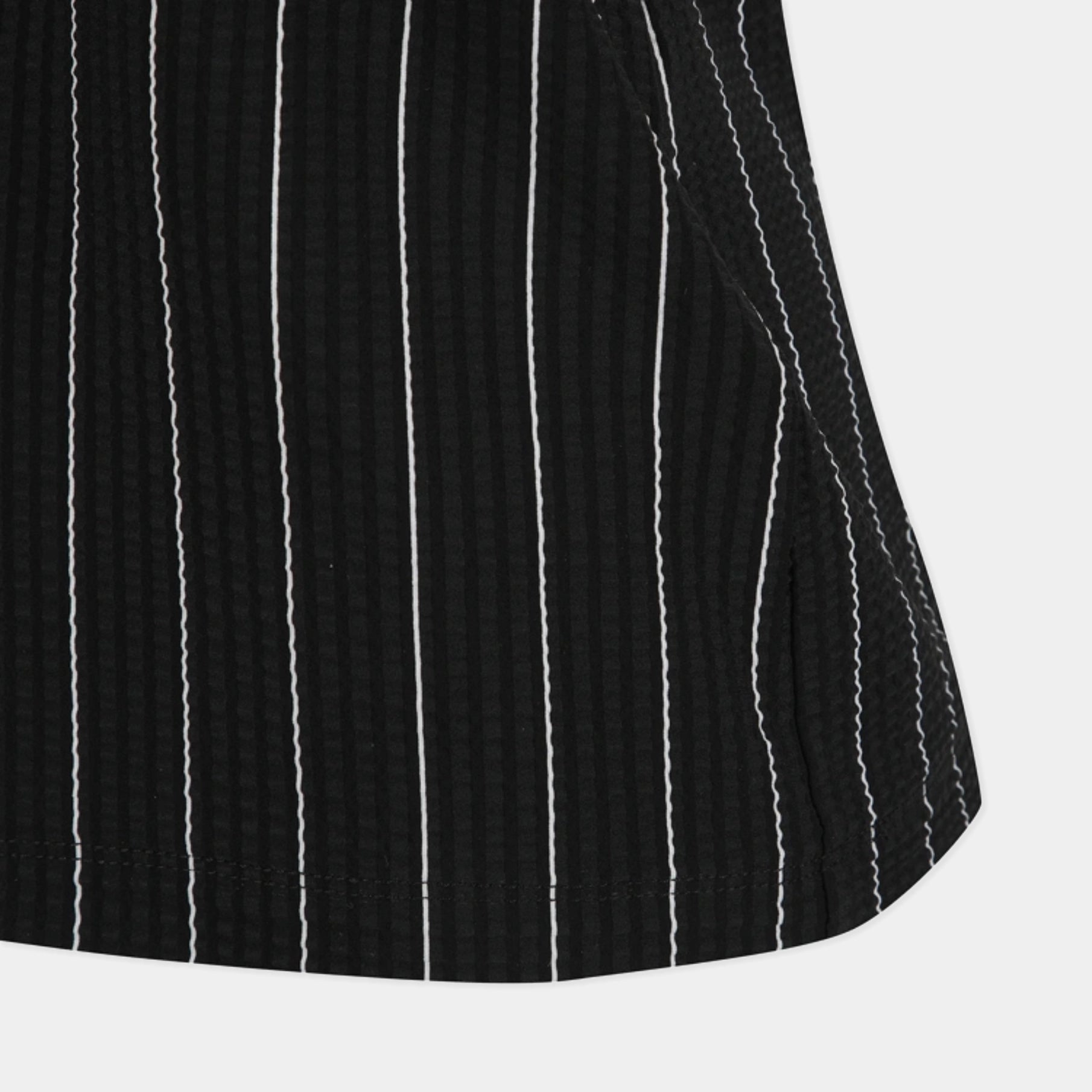 Close-up of a black textured fabric with vertical white pinstripes, showing the material texture and hem detail against a light gray background.