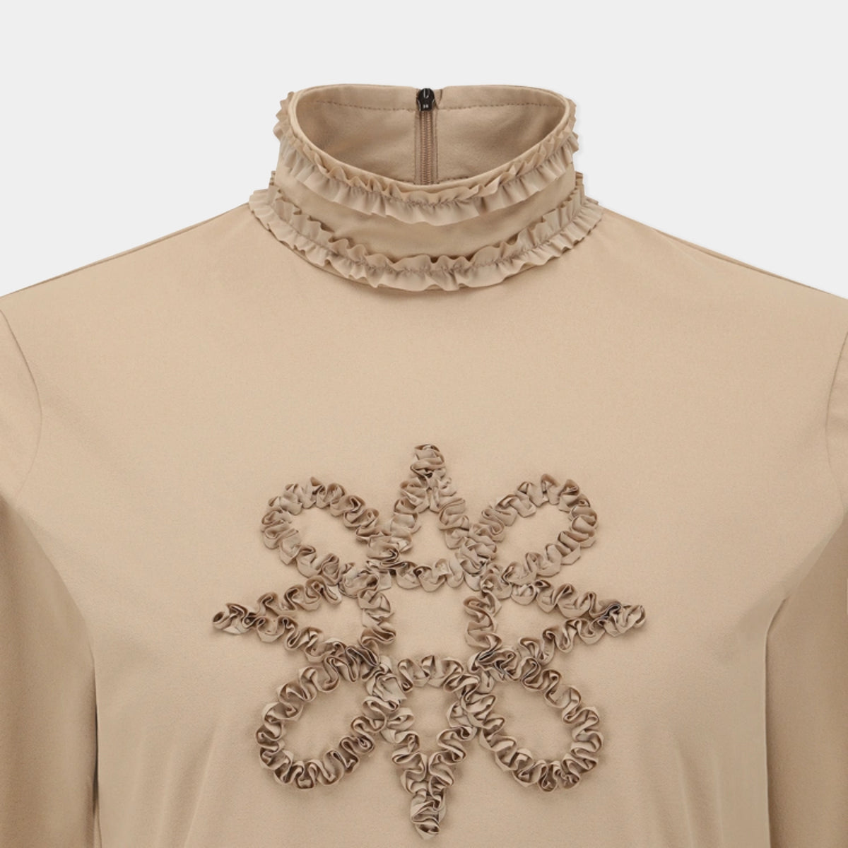Beige long-sleeve top with a high ruffled mock neck and a large textured floral applique on the chest, shown on a mannequin against a light gray background.