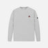 A light gray heather crewneck sweatshirt with a small embroidered patch on the left chest and a black sleeve tag, shown against a light gray background.
