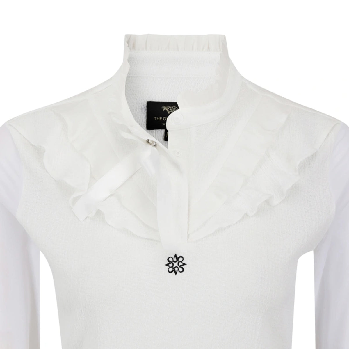 White long-sleeve blouse with a high ruffled mock neck collar, a matching ruffled bow at the neckline, and a small black floral emblem on the chest.