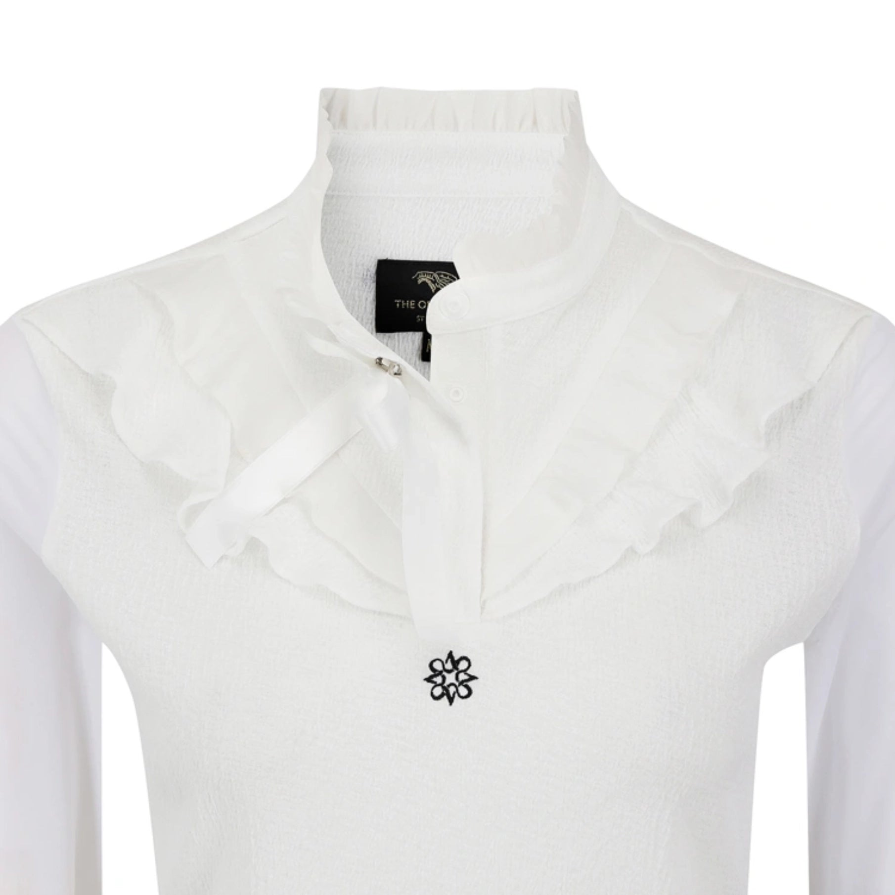 White long-sleeve blouse with a high ruffled mock neck collar, a matching ruffled bow at the neckline, and a small black floral emblem on the chest.