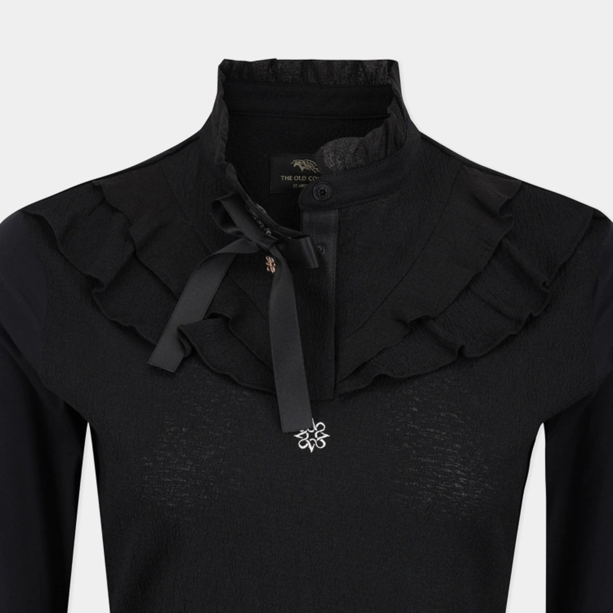 A close-up of a black long-sleeve top with a high ruffled collar, a black ribbon bow at the neck, and a small silver floral embellishment on the chest.