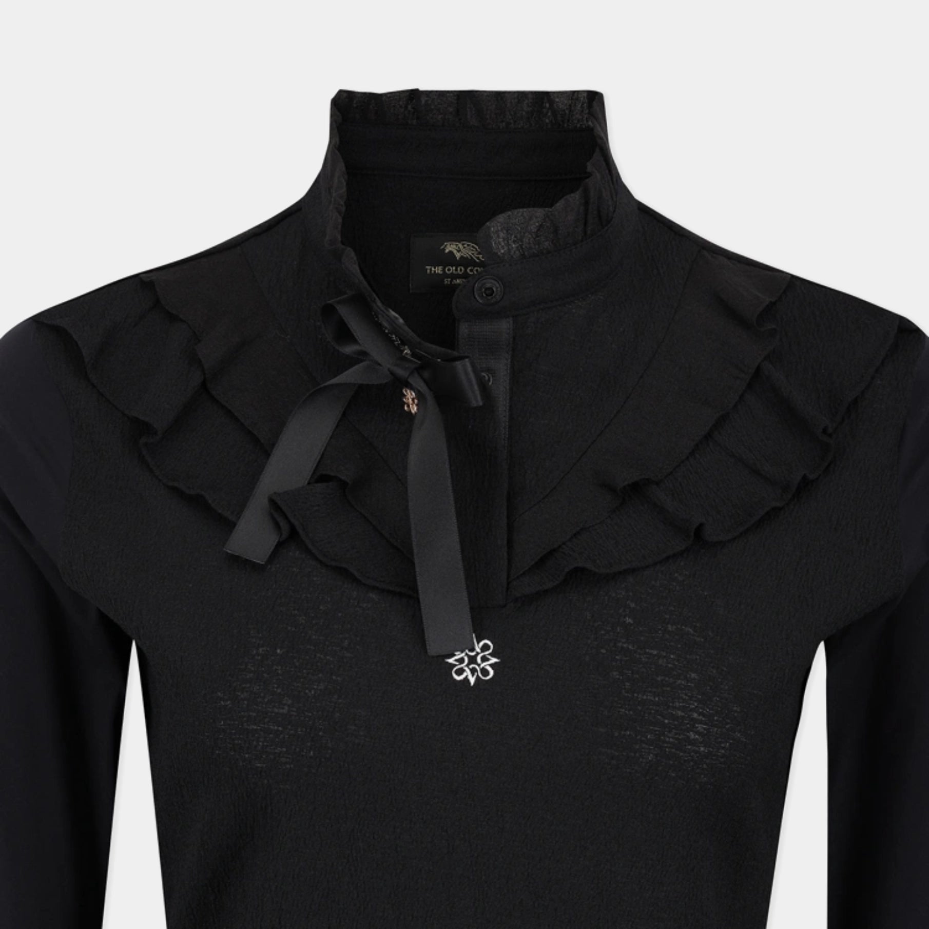 A close-up of a black long-sleeve top with a high ruffled collar, a black ribbon bow at the neck, and a small silver floral embellishment on the chest.