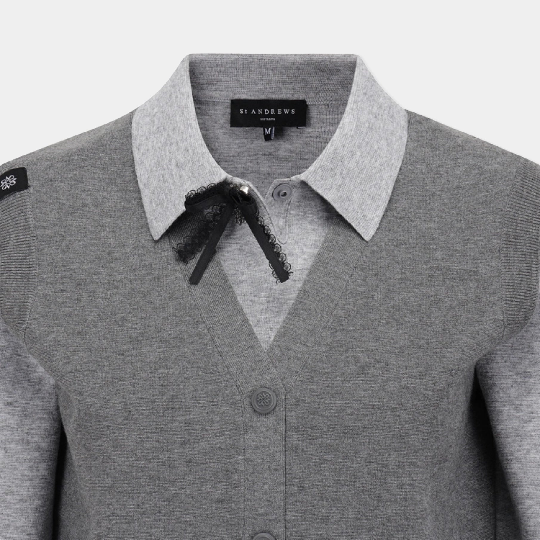 A close-up of a gray knit cardigan sweater featuring a contrasting light gray pointed collar with a black lace bow, and a black brand label reading 'SANDREMS' visible inside the collar.