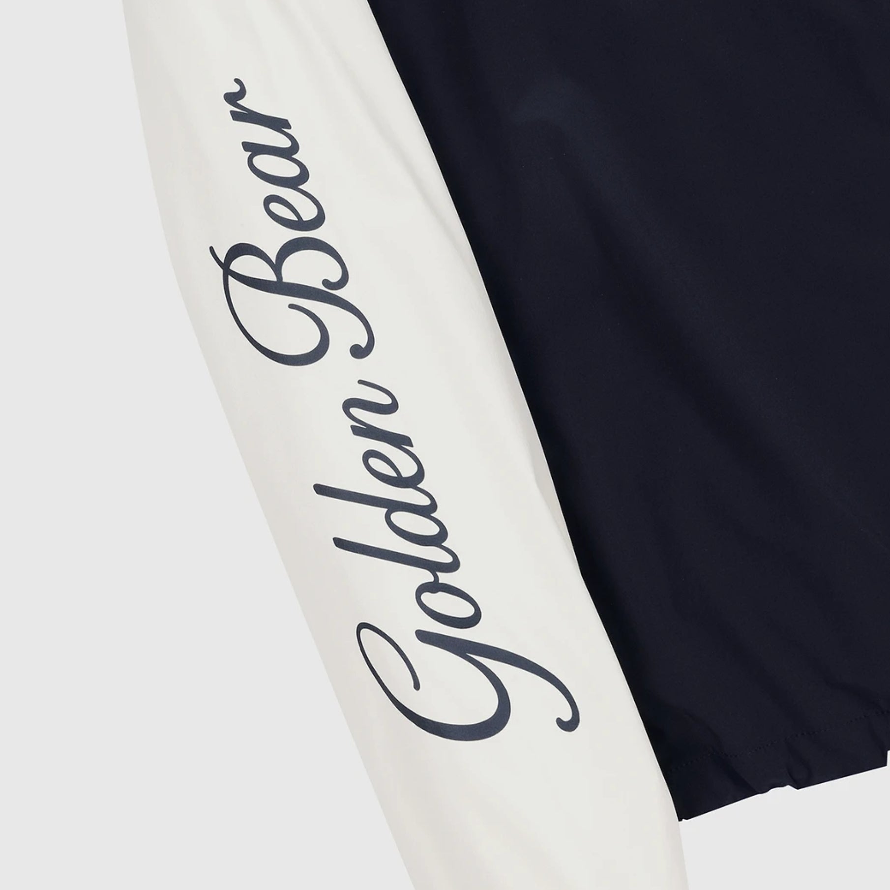 Close-up of a garment showing a white sleeve with large dark script reading 'Golden Bear' and a dark navy body panel, on a light gray background.