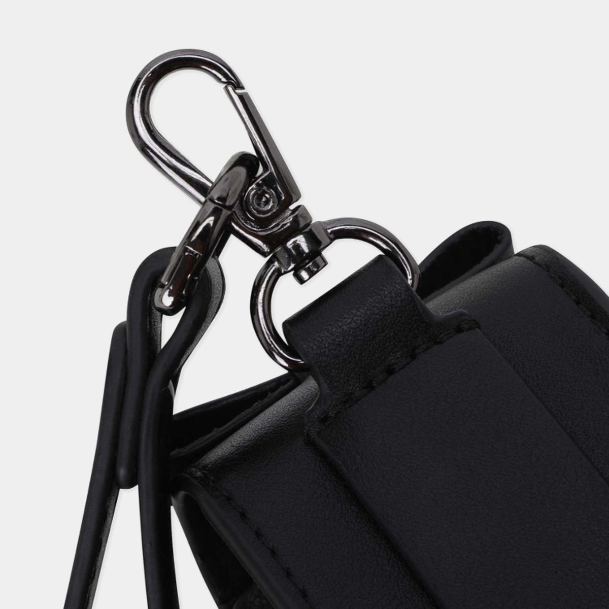 Close-up of a black leather or faux-leather bag with a black strap and a shiny silver metal carabiner clasp on a light gray background.