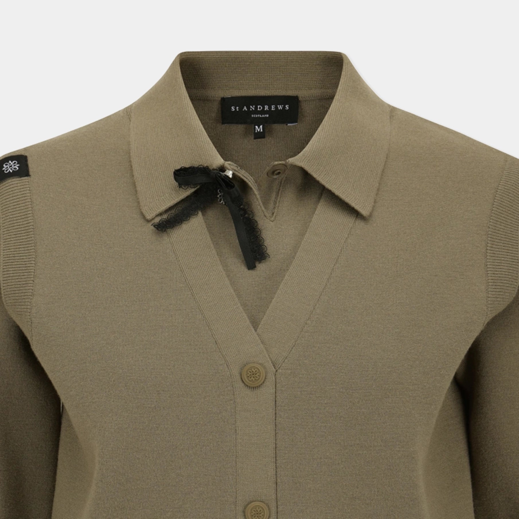 A close-up of a taupe knit cardigan sweater by St Andrews, featuring a pointed collar with a black ribbon bow, button-front closure, and ribbed sleeve panels.