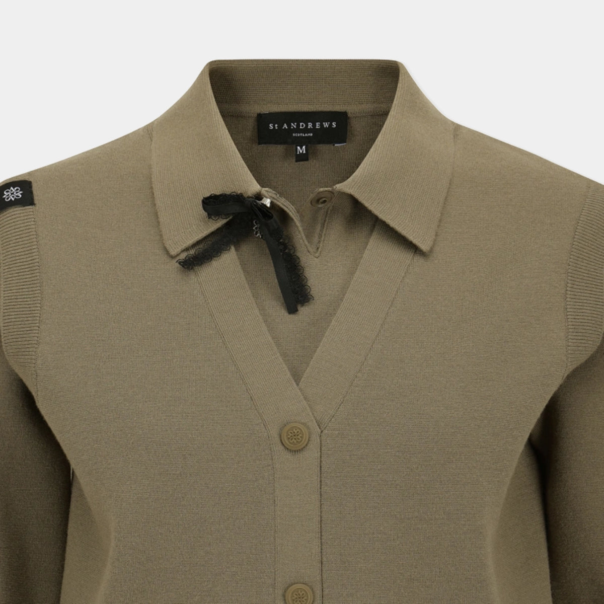 A close-up of a taupe knit cardigan sweater by St Andrews, featuring a pointed collar with a black ribbon bow, button-front closure, and ribbed sleeve panels.