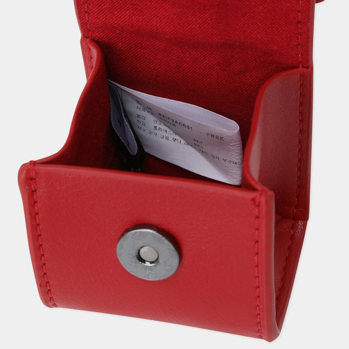 A close-up of a red leatherette card holder or wallet with a silver snap button on the front and a white paper insert inside.