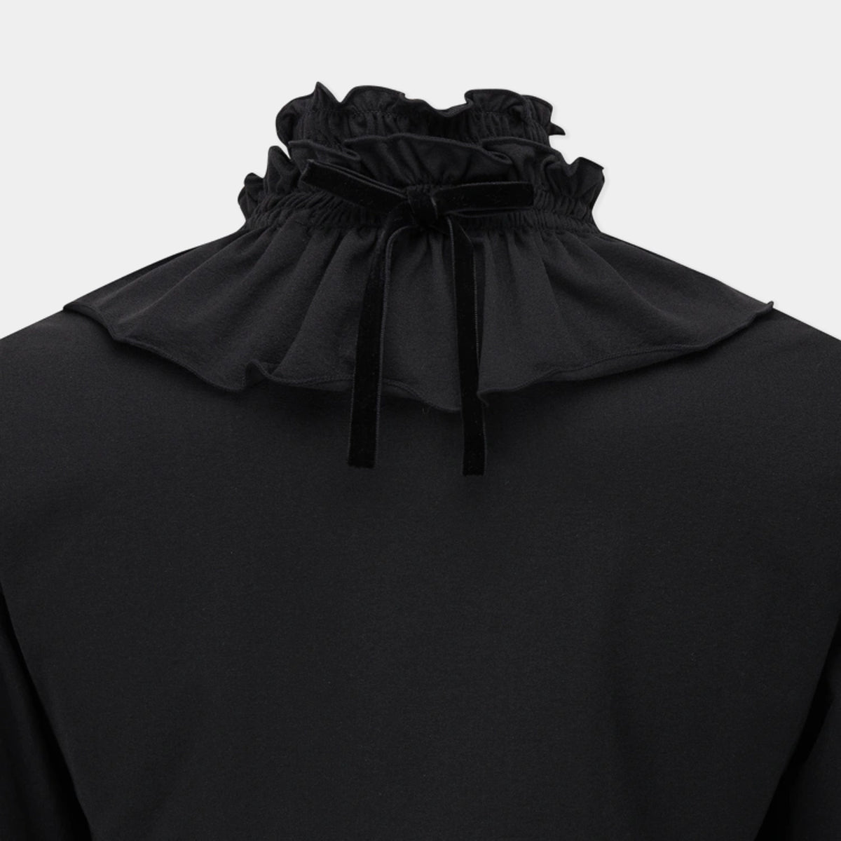A close-up of a black long-sleeve top featuring a high, gathered ruffled collar with a bow detail, set against a light gray background.